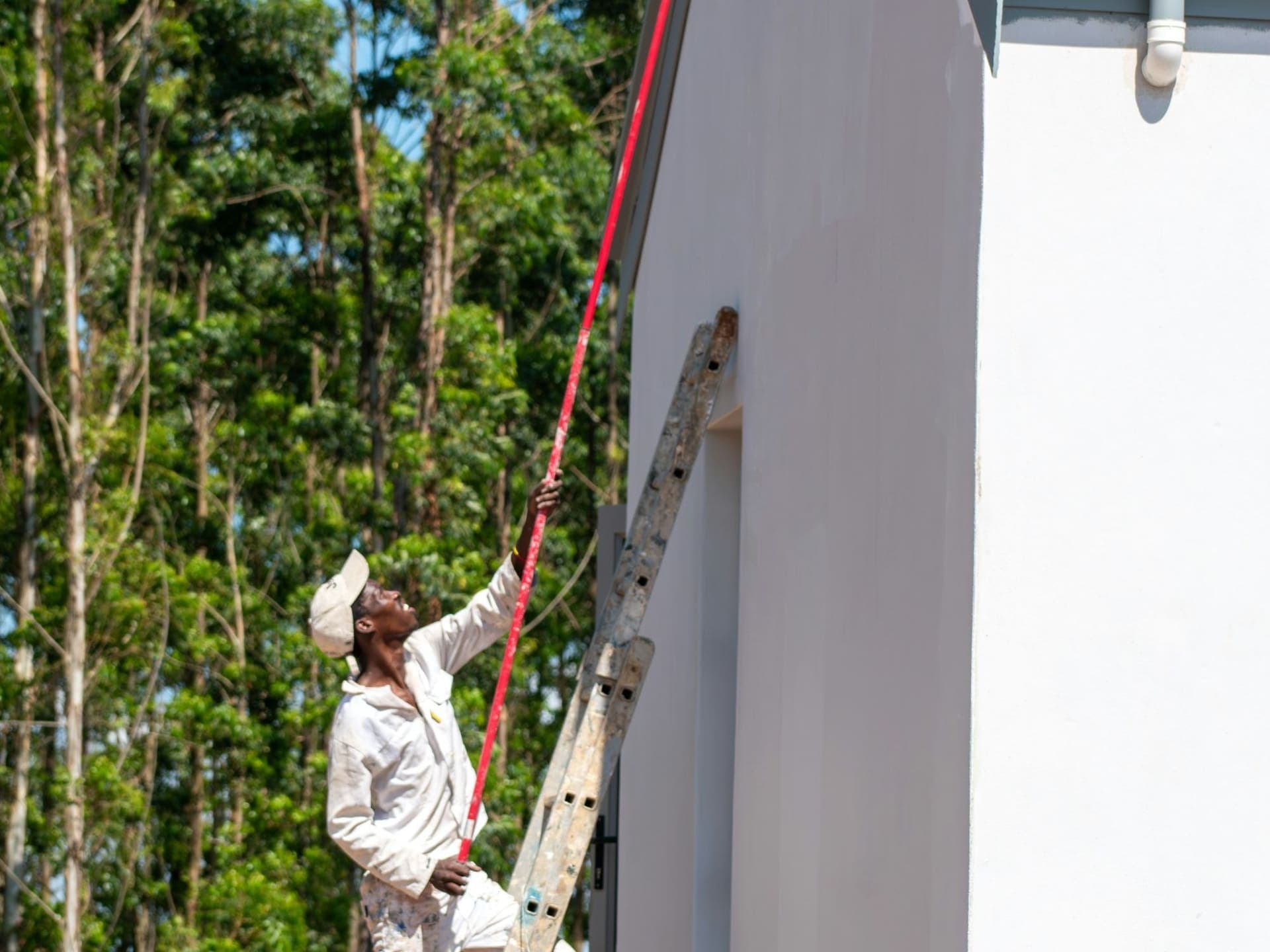 Painter on a ladder rolling paint onto the exterior wall of a house