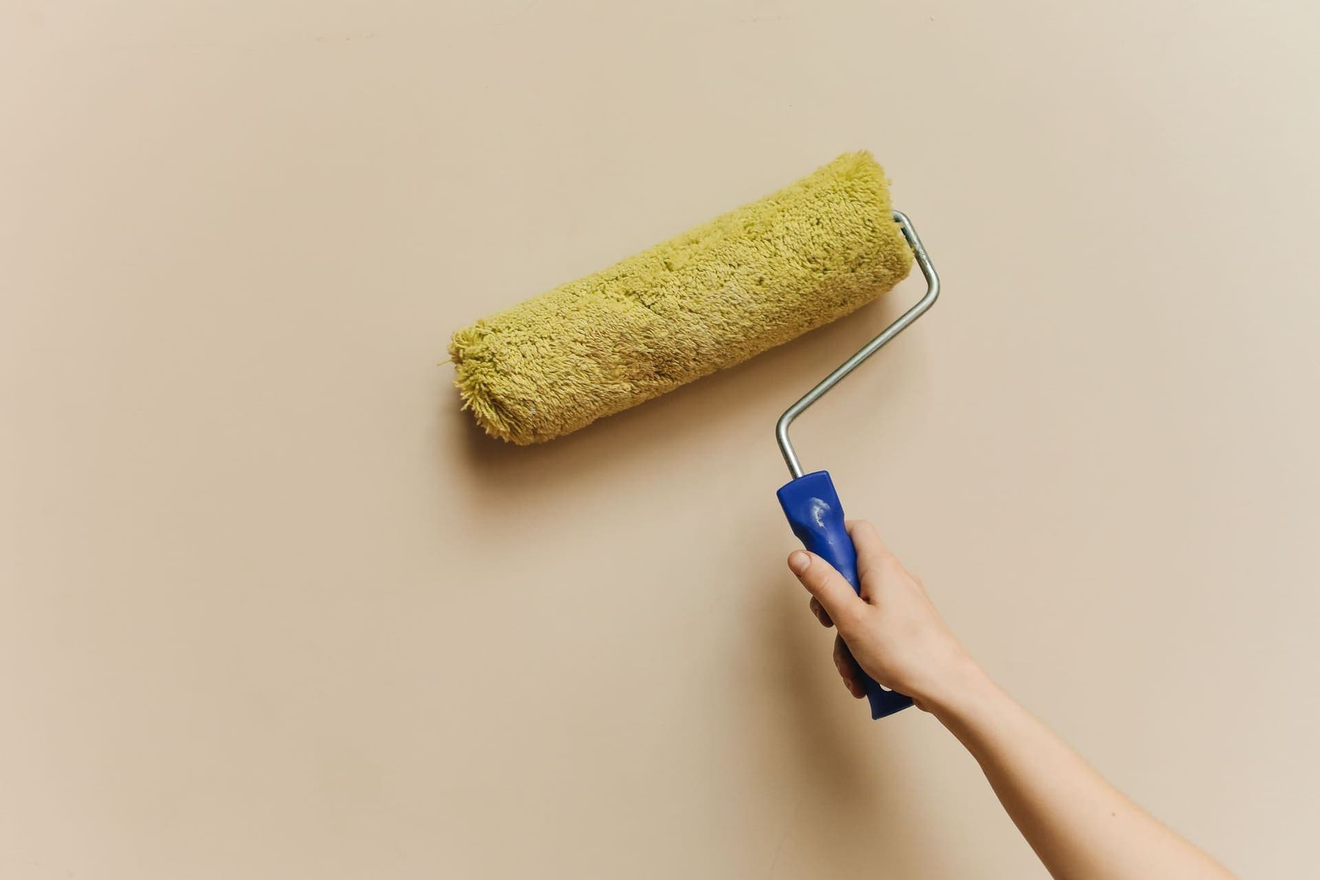 Hand rolling fresh paint onto a beige interior wall