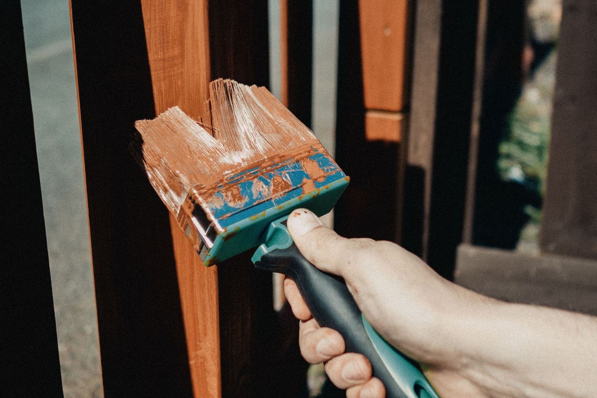 Hand brushing stain onto a wooden railing outdoors
